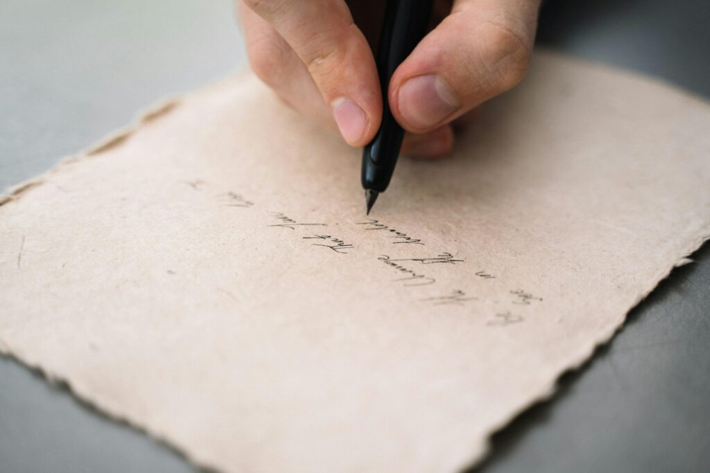 Someone writing a letter on handmade paper using a black pen.