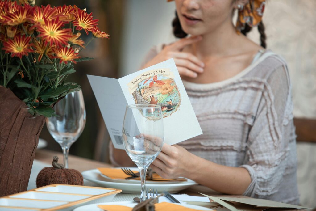 Lady reading a thank you card over a table, with flowers to her left. 