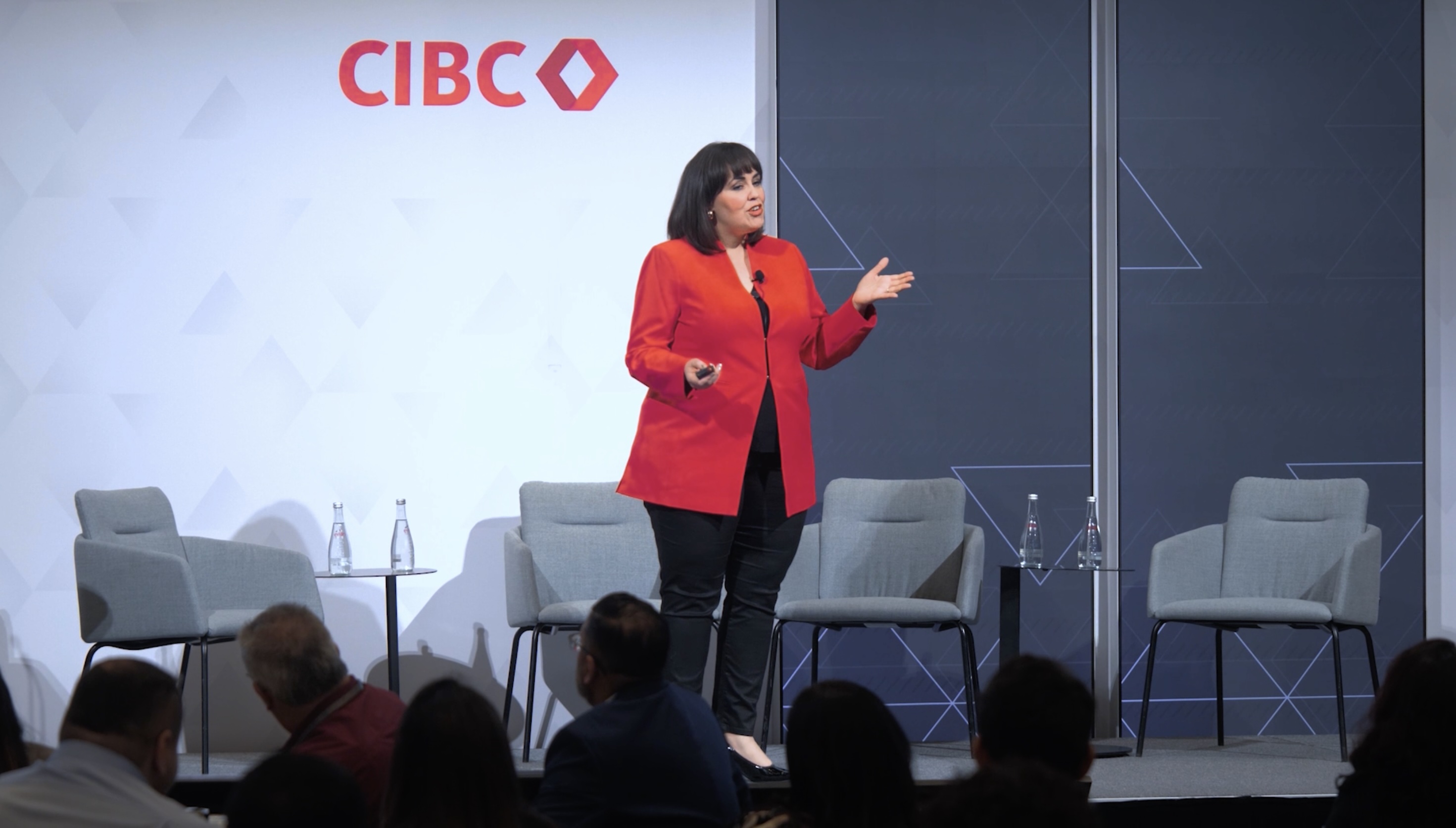 Lady in red jacked on stage public speaking, with CIBC Logo behind her